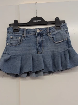 Blå jeanskjol med volang - Trendig blå jeanskjol med volang nertill och klassiska jeansdetaljer som fickor fram och bak. Kjolen har en kort passform och är tillverkad i denim med råa kanter för en cool look. Har gjort den själv av ett par jeans från Gina Tricot i storlek 146 men skulle säga att kjolen passar mig som vanligtvis bär xs/158. Går även att sjustera i midjan. 