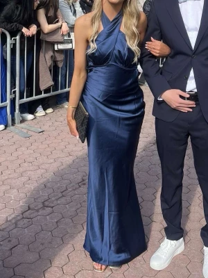 Marinblå långklänning i satin - Marinblå balklänning i satinliknande material. Går hela vägen ner till marken och lite till på mig som är ca 168. Har använts en gång på min bal och har inga deffekter. Är öppen i ryggen med rosettknytning som man kan justera själv. Helt slutsåld på hemsidan!