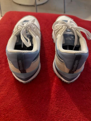 Vita och blå Reebok sneakers - Säljer ett par fräscha vita och ljusblå sneakers från Reebok. Skorna har klassisk låg modell med ovandel i textil och mockadetaljer, samt vita snören och Reebok-logga på hälen. Snygg retrostil som passar till många outfits.