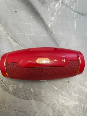 Röd bärbar högtalare med guldknappar - Snygg röd bärbar högtalare från Hopestar med guldfärgade knappar och detaljer. Högtalaren har rundad form, metallgaller och tydliga kontrollknappar för volym, samtal och musik. Perfekt för att ta med sig överallt tack vare det smidiga handtaget.