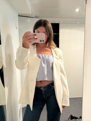 Vit oversized kavaj med knappar - Stilren vit kavaj i oversized modell med raka axlar och tre knappar framtill. Klassisk krage och långa ärmar. Passar perfekt till jeans eller kjol för en trendig look. Materialet ser ut att vara en mjuk och slät textil.