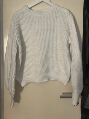 Vit ribbstickad tröja - Klassisk vit stickad tröja med ribbad struktur och rund hals. Tröjan har långa ärmar och breda muddar vid ärmslut och nederkant. Perfekt för lager på lager och enkel att matcha med olika stilar.