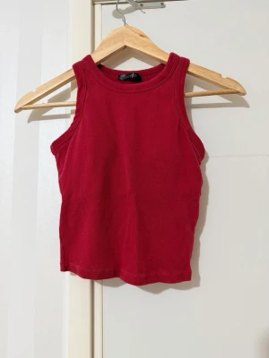 Vinröd ribbad linnetopp - Snygg röd ribbad linnetopp med rund halsringning och ärmlös design. Perfekt för varma dagar eller som layering-piece. Tidlös modell som är enkel att matcha med olika stilar.