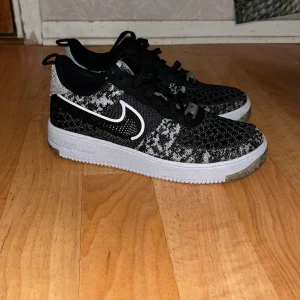 Nike Air Force 1 Flyknit svart/vit - Säljer ett par Nike Air Force 1 Flyknit sneakers i svart och vitt. Ovandelen är i stickat material med ett mönster i svart och vitt, vit sula och klassisk Nike Swoosh på sidan. Skorna har svarta skosnören och detaljer i plast framtill. Priset kan diskuteras vid snabbaffär