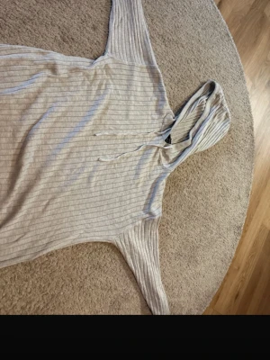 Ljusgrå ribbad hoodie med huva - Säljer en ljusgrå hoodie med tunna vertikala ränder och huva med dragsko. Hoodien är tillverkad i ett mjukt, stretchigt material och har en avslappnad passform. Perfekt för chill dagar eller när du vill ha något bekvämt och stilrent.