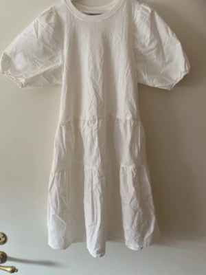 Vit volangklänning med puffärm - Säljer en vit klänning med puffärmar och volangdetaljer. Klänningen har rund halsringning och är sydd i ett mjukt bomullstyg. Passformen är loose och längden går till knäna. Perfekt för sommarens alla tillfällen!