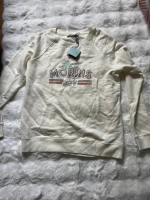 Vit sweatshirt Morris Lady - Säljer en stilren vit sweatshirt från Morris Lady med tryck framtill.Tröjan har rund halsringning, långa ärmar och mjukt material som känns skönt mot huden. Perfekt för en avslappnad och trendig look. Stilen 