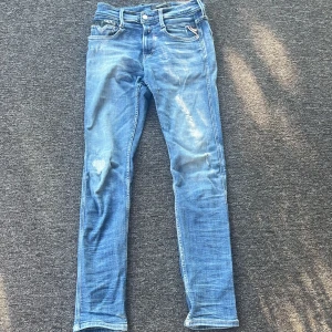 Replay Anbass skinny jeans blå - Säljer ett par Replay Anbass jeans i skinny fit med snyggt slitna detaljer och klassisk femficksdesign. Jeansen är ljusblå med inslag av mörkare tvätt och har låg midja. Perfekta för dig som gillar en tight och modern look.