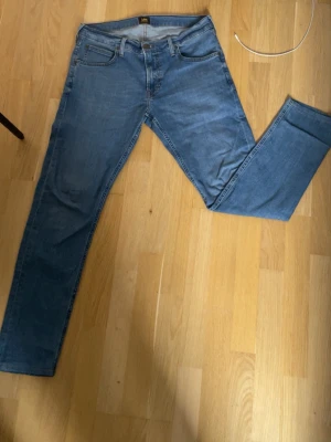 Blå  jeans från Lee - (Går att pruta vid snabb affär) Säljer ett par klassiska blå jeans från Lee med rak passform. Jeansen har fem fickor, bälteshällor och knappgylf. Materialet är mjukt denim i bomull och färgen är ljusblå. Perfekta till en avslappnad stil.  W31 L32 
