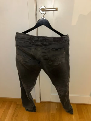 Replay Hyperflex - Säljer ett par grå jeans från replay med klassisk femficksdesign och diskreta sömmar på bakfickorna. Jeansen har en något tvättad look och raka ben. Materialet är mjukt denim som ger en avslappnad känsla. Perfekta för dig som gillar streetwear och enkel stil.