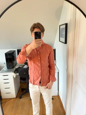 Rosa/orange linneskjorta från These glory days - Säljer en snygg skjorta från These glory days i 100% linne. Skjortan har klassisk krage, vita knappar och lång ärm. Det följer även med 2 extra knappar. Hör gärna av dig vid frågor!