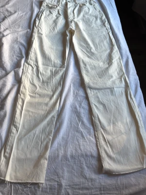 Vita raka jeans med rå kant - Säljer ett par vita jeans med rak passform och råa, fransiga benslut. Jeansen har klassisk femficksdesign och hög midja. Perfekta för dig som gillar en clean och avslappnad stil. Materialet är kraftig denim i bomull.