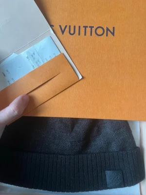 Svart mössa från Louis Vuitton - Snygg svart mössa från Louis Vuitton med ribbad kant och diskret logotypmärke framtill. Tillverkad i mjukt material som känns lyxigt och passar perfekt till höst och vinter. En stilren accessoar för dig som gillar exklusiva detaljer.