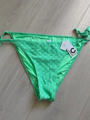 Gröna bikiniunderdelar Cubus - Snygga gröna bikiniunderdelar från Cubus med rutigt mönster och knyt i sidorna. Materialet känns mjukt och har en cool struktur som sticker ut på stranden. Perfekt för dig som vill ha en färgstark och trendig look till sommaren.