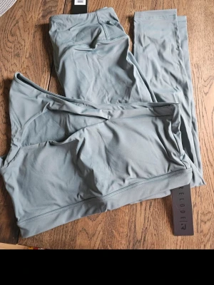 Relode Träningsset lumi Tights & Top Grön XL - Set med träningstights och matchande sport-bh. Tightsen har en smickrande passform. Sport-bh:n har en unik design med en axel och utskuren detalj både framtill och baktill. Båda plaggen är designade för att ge komfort och stil under träningspasset. Nya med lappar kvar i förpackning.   Nypris sport bh 399kr Nypris tights 599kr