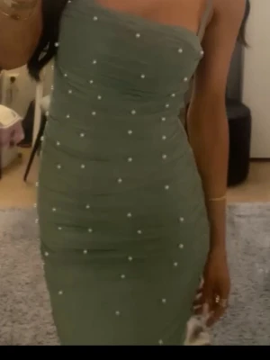 Grön  klänning med pärlor - Trendig grön klänning med smala axelband och dekorativa pärlor över hela tyget. Klänningen har en figurnära passform och är perfekt för dig som vill sticka ut. Materialet ser ut att vara polyester.