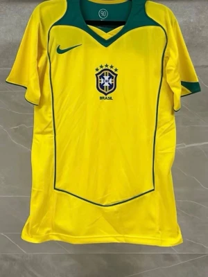 Brasilien fotbollströjor gul Nike & Umbro - Två klassiska Brasilien fotbollströjor i gult med gröna detaljer. Ena tröjan från Nike med modern design och V-ringning, den andra från Umbro med krage och retrostil. Båda har CBF-emblemet på bröstet. Perfekta för fotbollsfans!