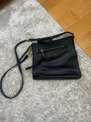 Svart axelväska Marc Jacobs läder (kom med pris förslag!!) - Snygg svart axelväska från Marc Jacobs i mjukt, strukturerat läder. Väskan har justerbar axelrem, guldfärgade metalldetaljer och en dragkedjeficka framtill. Perfekt storlek för det viktigaste och stilren design som funkar till allt.