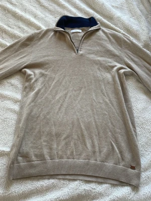 Beige halvzip-tröja från Mango - Snygg beige tröja från Mango med halvzip och hög krage. Insidan av kragen är mörkblå vilket ger en schysst kontrast. Tröjan har ribbade muddar och är perfekt för lager-på-lager-stil. Materialet känns mjukt och bekvämt.