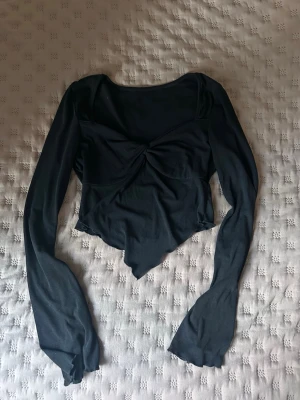 Svart långärmad topp från SHEIN - Svart långärmad topp från SHEIN med snygg twistad detalj framtill och asymmetrisk nederkant. Toppens material är mjukt och stretchigt.
