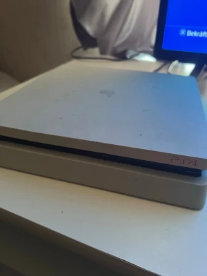 Vit PlayStation 4 Slim konsol - Säljer en vit PlayStation 4 Slim från Sony. Konsolen har en stilren, platt design med rundade hörn och PS4-loggan på ovansidan. Tillverkad i plast och passar perfekt för gaming och streaming.