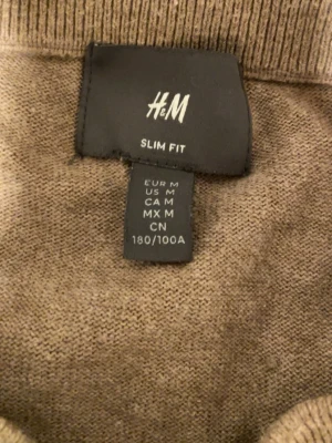 Beige slim fit stickad tröja H&M - Säljer en beige stickad tröja från H&M i slim fit-modell. Tröjan har en enkel och stilren design med rund halsringning och ribbade muddar. Perfekt för lager-på-lager och passar till många olika outfits.
