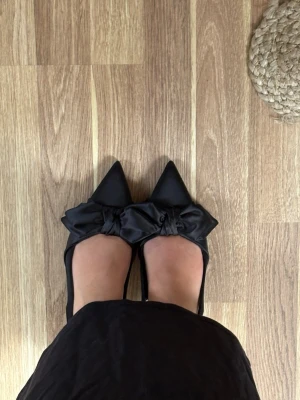 Svarta pumps/klackar med stor rosett (aldrig använda och i original kartong) - Stilrena svarta pumps/klackar med 5 cm klack. Storlek 38. Aldrig använda och kommer i original kartong (jag har flera svarta klackar så bestämde mig för att sälja dessa då jag aldrig fått användning för dem). Skorna har en rosett framtill och är tillverkade i ett glansigt tygmaterial. Super eleganta och snygga till både kjol och jeans. Väldigt enkla att gå i då de sitter fast i hälen. Märke Catwalk. Original priser var 599kr. 