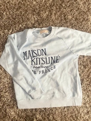Riktigt fett Ljusblå sweatshirt Maison Kitsuné🤩🙌 - Snygg ljusblå sweatshirt från Maison Kitsuné med tryck i mörkblått framtill. Tröjan har rund halsringning, långa ärmar och ribbade muddar vid ärmslut och nederkant. Perfekt för en avslappnad och trendig look.🤩🙌