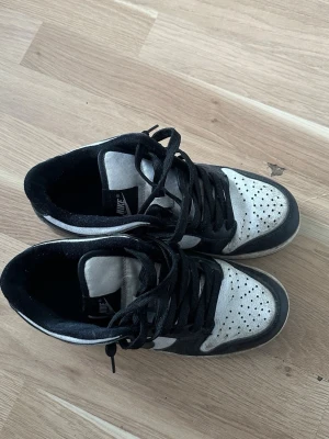Nike dunk panda svartvita sneakers låga - Nike sneakers i svart och vitt med klassisk swoosh på sidan. Lågt skaft, svart sula och svarta skosnören. Ovandelen är i mocka och textil med perforerade detaljer på tån för extra ventilation. Perfekta för en streetwear-look.