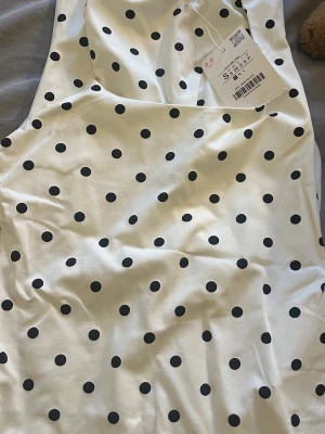 Vit prickig linnetopp från Sinsay - Supersöt vit linnetopp från zara med svarta prickar. Toppen är ärmlös och har en klassisk rak passform, perfekt för att skapa en fräsch och trendig look. Tillverkad i mjuk bomull som känns skön mot huden.