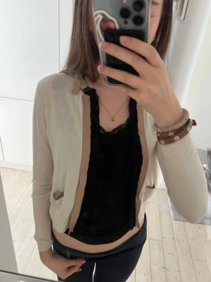 Beige kofta med bruna detaljer - Snygg beige kofta med bruna kanter och små fickor framtill. Koftan har långa ärmar och en öppen design utan knappar. Perfekt att slänga över ett linne eller t-shirt för en chill och stilren look.