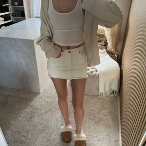Vit jeanskjol från Levis  - Snygg vit jeanskjol med rå, fransad kant nertill och klassiska fem fickor. Kjolen har bälteshällor och stängs med knapp och dragkedja framtill. Perfekt för en trendig och avslappnad look. Köpt på Plick men aldrig använd av mig!! Vet ej var den är köpt eller om de är en original💕💕