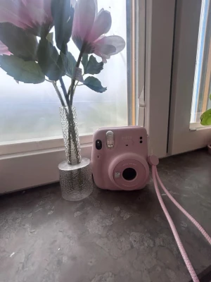Rosa Fujifilm Instax Mini 11 kamera - Säljer en söt rosa Fujifilm Instax Mini 9 direktbildskamera. Kameran har en rund form, inbyggd blixt och en matchande handledsrem. Perfekt för att ta instant-bilder med vänner och samla minnen direkt på papper.