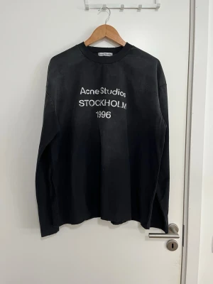 Svart långärmad  Acne Studios M - Cool svart långärmad tröja från Acne Studios med vit text 'Acne Studios STOCKHOLM 1996' på bröstet. Tröjan har rund halsringning och avslappnad passform, perfekt för en trendig streetwear-look.