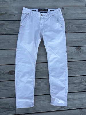 Vita chinos från Jacob Cohen - Snygga vita jeans från Jacob Cohen med klassisk femficksmodell och raka ben. Jeansen har silverfärgade nitar och knapp, samt bälteshällor. Tillverkade i ett mjukt och bekvämt material som passar perfekt till en trendig look.