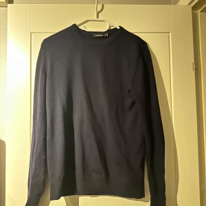 Mörkblå tröja från J.Lindeberg - Säljer en stilren mörkblå tröja från J.Lindeberg. Storlek M men sitter som S då den krympt lite i tvätten. Tröjan har en klassisk design med långa ärmar och rund hals. Perfekt för en elegant och avslappnad look.