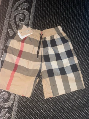 Burberry badshorts / swim shorts – Strl L/M - Säljer ett par snygga Burberry shorts med klassiska Nova Check-rutorna. Storlek L men passar även M beroende på hur man vill att de ska sitta. Elastisk midja med snörning för bra passform.  * Märke: Burberry * Storlek: L (passar även M) * Skick: Helt nya med tags kvar * Färg: Beige/rutig * Perfekta till sommaren, stranden eller vardagsbruk  Skriv vid frågor eller för fler bilder 📩 Skickas snabbt och säkert 📦