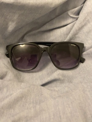 Svart/lila Wayfarer solglasögon - Klassiska svarta solglasögon i Wayfarer-modell med breda bågar och mörka glas. Snygg och tidlös design som passar till de flesta outfits. Perfekta för soliga dagar och ger en cool vibe.