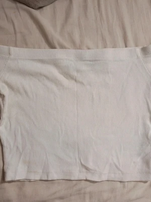 Vit ribbad tubtopp - En stilren vit ribbad tubtopp i stretchigt material. Toppen är axelbandslös och har en croppad passform som passar perfekt till höga jeans eller kjol. Enkel att matcha och superbekväm för varma dagar.