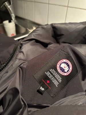 Svart dunjacka från Canada Goose - Säljer en svart dunjacka från Canada Goose med klassisk logga på insidan. Jackan är fylld med äkta dun och har en stilren design med dragkedja. Perfekt för kalla vinterdagar och håller dig varm hela säsongen. Kan tänkta mig gå ner i pris då jag inte har kvitto men inga skam bud!