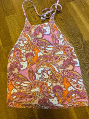 Mönstrad linnetopp från Bik Bok - Färgglad linnetopp från Bik Bok med paisleymönster i rosa, orange och vitt. Toppen har tunna axelband som knyts i nacken och är perfekt för varma dagar. Materialet är mjukt och lätt, vilket gör den superbekväm att bära.