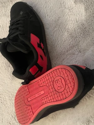 Svarta DC sneakers med röda detaljer - Säljer ett par riktigt snygga DC skor i svart med röda detaljer och röd sula som sticker ut fett. Skorna har en clean streetwear/skate-look och passar perfekt till både baggy jeans, cargos, hoodie eller tracksuit. Funkar lika bra till vardags som för att få en outfit att poppa lite extra. De är bekväma, stabila och har den klassiska DC-stilen med chunky känsla och cool design. Den röda sulan ger skorna en unik touch som verkligen syns. Köptes för 700 kr!! ‼️PRIS KAN DISKUTERAS‼️