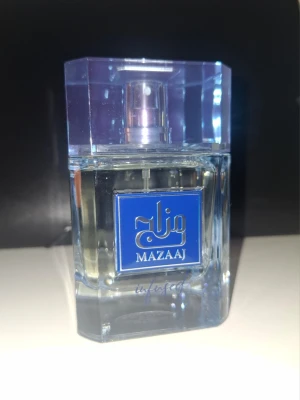 Mazaaj Infused - En stilren parfym från Mazaaj med en transparent glasflaska och blå etikett. Flaskan har en fyrkantig form och ett lila transparent lock. Perfekt för dig som gillar snygg design och vill ha en unik doft i samlingen.