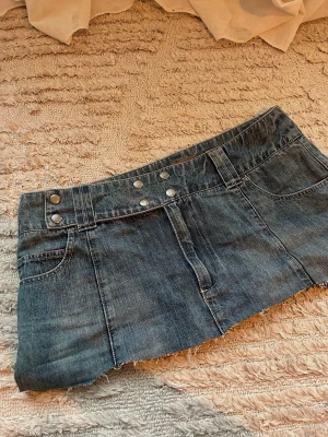 Lågmidjad mörkblå vintage jeanskjol  - Trendig mörkblå jeanskjol i kort modell med rå, avklippt kant. Vintage, passar st 38-40. Använd fåtal gånger. Lågmidjade minikjol