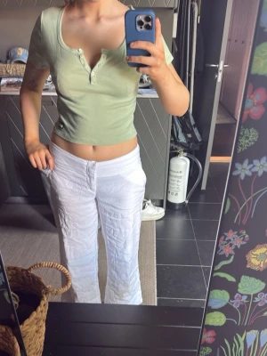 Ljusgrön croppad topp med knappar - Snygg ljusgrön croppad topp med korta ärmar och knappdetaljer framtill. Toppen har en djupare rundad ringning och är i ett mjukt, stretchigt material. Perfekt för dig som gillar en enkel men trendig stil.