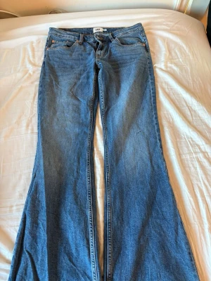 Blå utsvängda jeans med hög midja - Säljer ett par klassiska blå jeans med utsvängda ben och hög midja. Jeansen har fem fickor och stängs med dragkedja och knapp. Perfekta för dig som gillar retrostil och vill ha ett par bekväma jeans i bomull. Passar även S