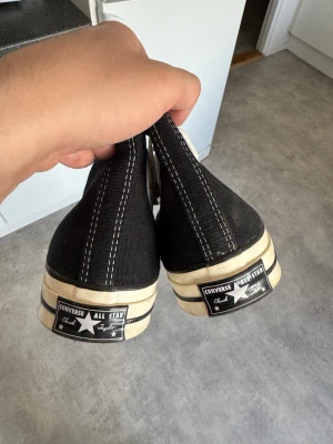 Svarta Converse All Star sneakers - Klassiska svarta Converse All Star high top sneakers med vit sula och vita snören. Skorna har tydliga kontrastsömmar och den ikoniska loggan baktill på hälen. Tillverkade i slitstark canvas och passar perfekt till en avslappnad streetstil.