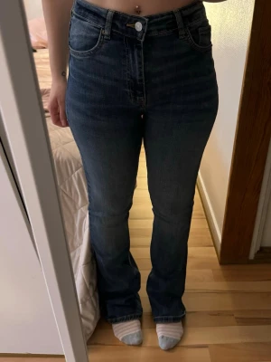 Mörkblå bootcut jeans med hög midja från Zara - Säljer ett par mörkblå bootcut jeans med hög midja och klassiska fem fickor. Jeansen har en snygg tvätt och raka ben som går ut lite nedtill. Har bara använt några gånger 