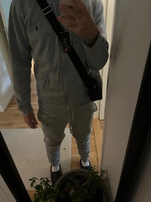 Grå tracksuit från Polo Ralph Lauren - Säljer en grå tracksuit från Polo Ralph Lauren med dragsko i midjan och ribbade benslut. Klassisk logga broderad på benet och mjukt material som känns riktigt skönt. Perfekta för chill dagar eller när du vill vara bekväm.