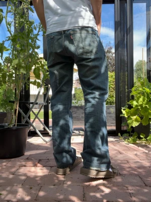 Blå raka jeans från Levi's 501 - Säljer ett par klassiska blå jeans från Levi's med raka ben och femficksmodell. Jeansen har en snygg tvättad look och tydliga sömmar. Tillverkade i slitstarkt denim med den ikoniska läderlappen bak i midjan. Det står att dem är L34 men det stämmer inte längden är 99cm